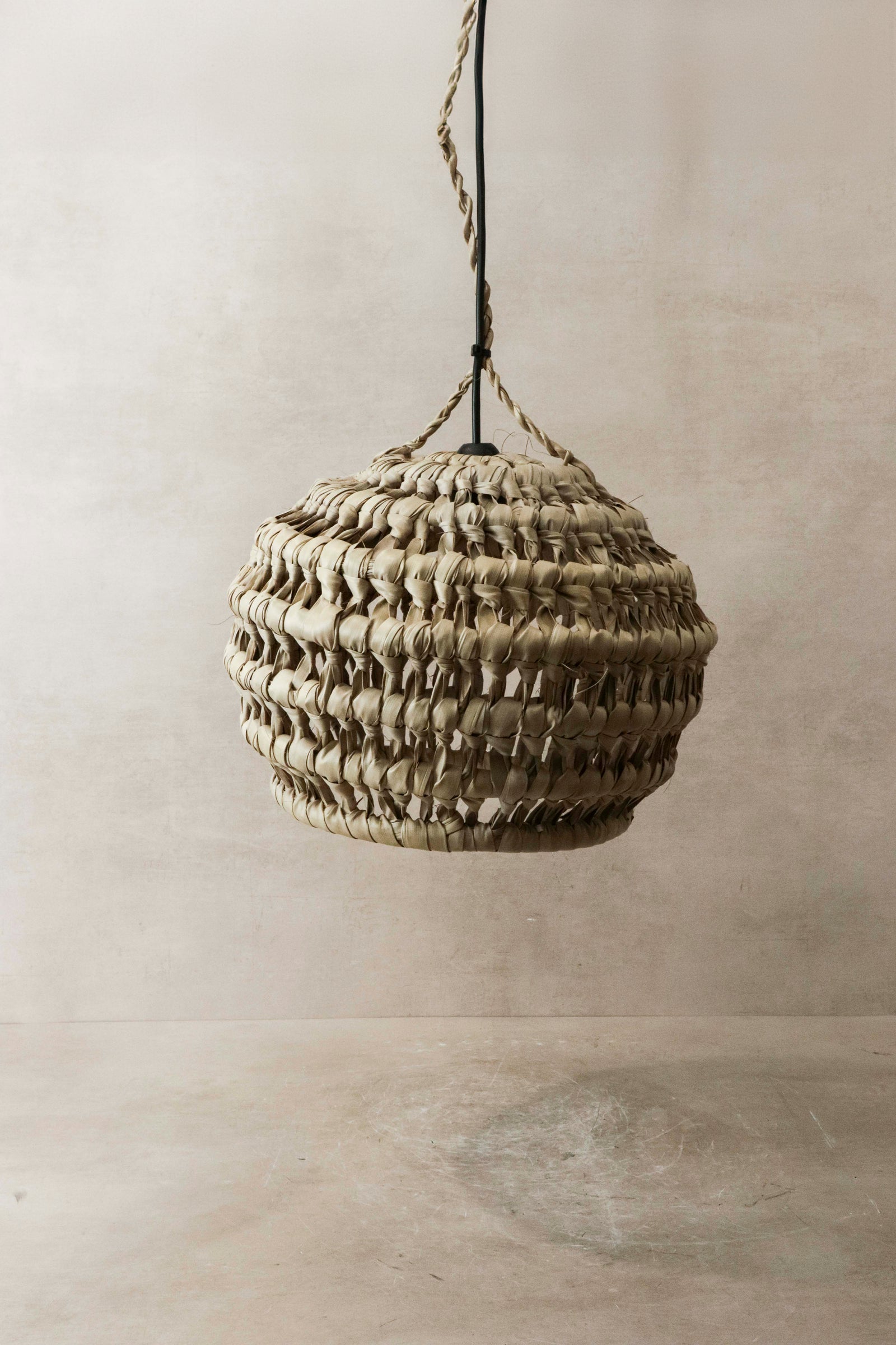 Palm leaf pendant shade — lit, showing the dappled glow